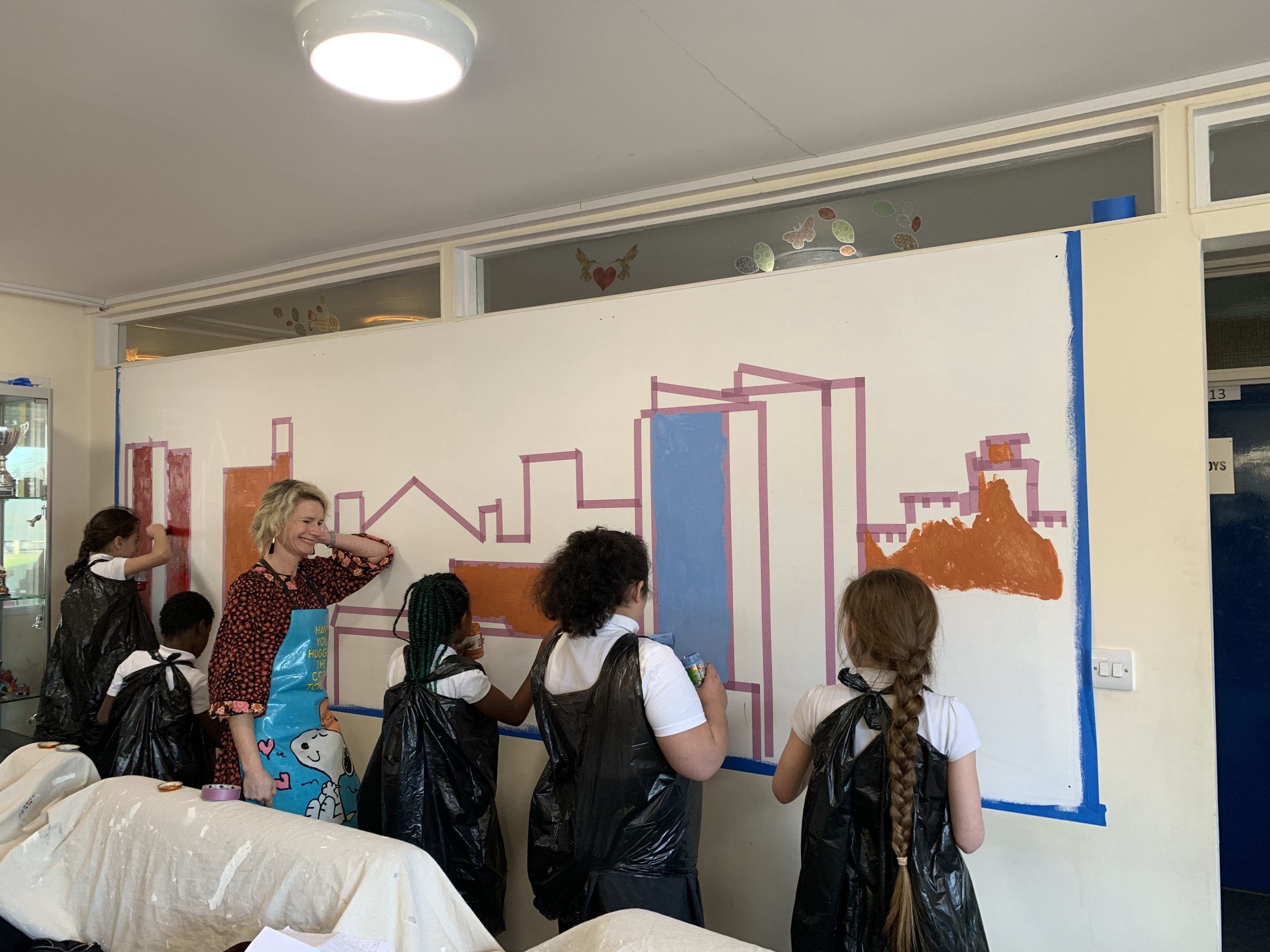 Teacher and schoolchildren painting a wall mural